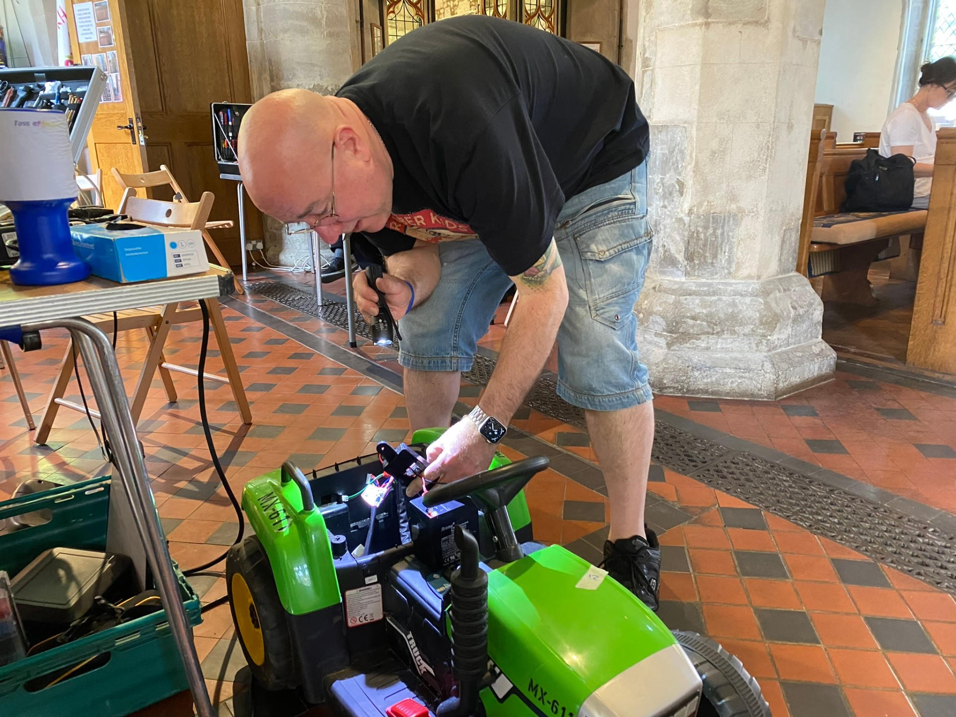 A volunteer repairing a child's electric ride-on tractor